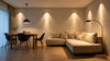 A cozy living-dining area with warm lighting. It features a beige sectional sofa, a wooden dining table with black chairs, and a floor lamp, creating a serene ambiance.